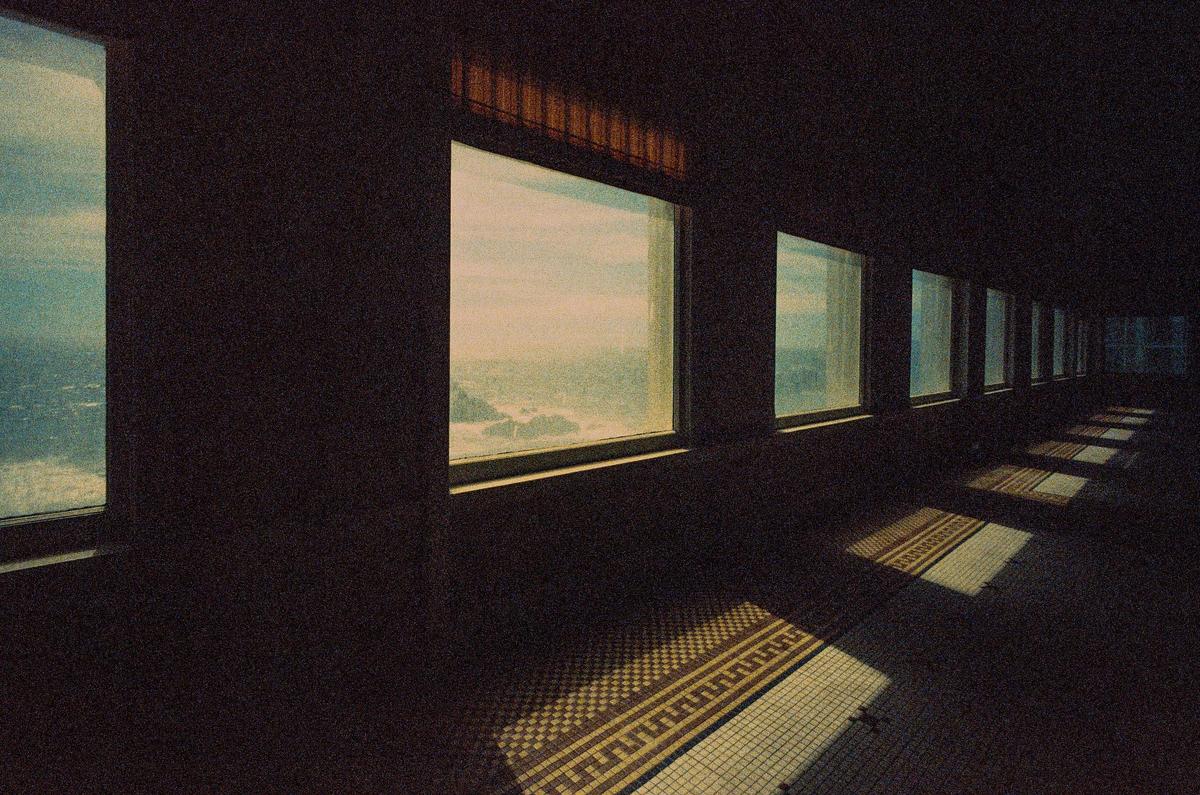 Sunlight streams through a row of windows onto a tiled floor in an abandoned diner.