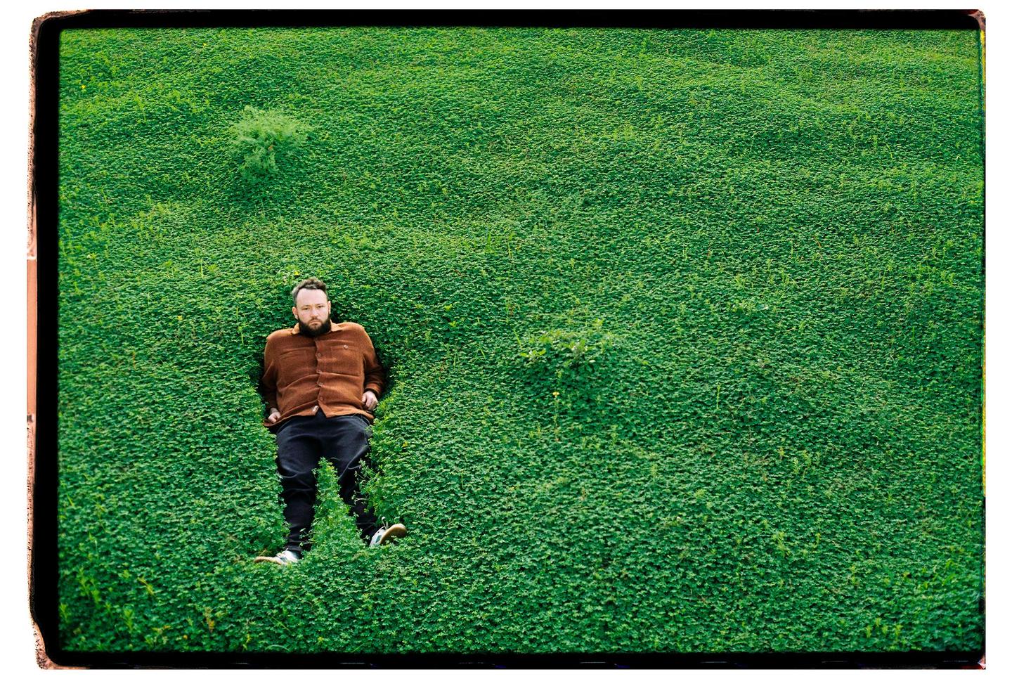 A man is lying on his back in a field of green clover.