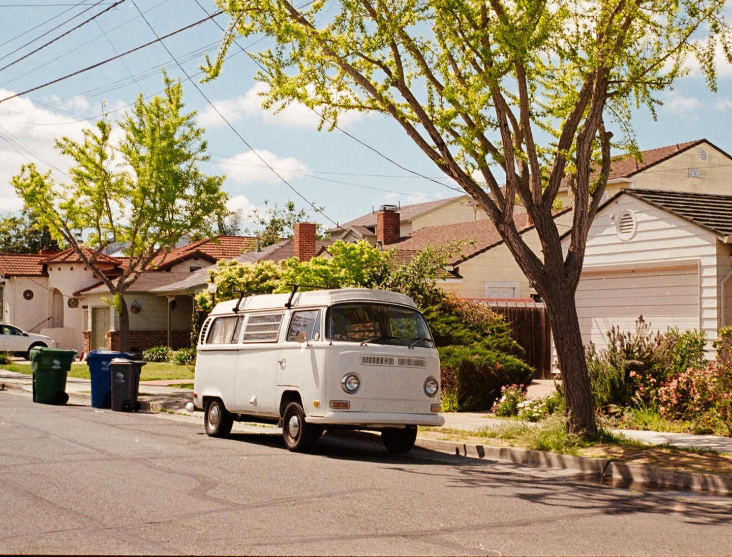 A white van is parked on a residential street lined with houses and trees.