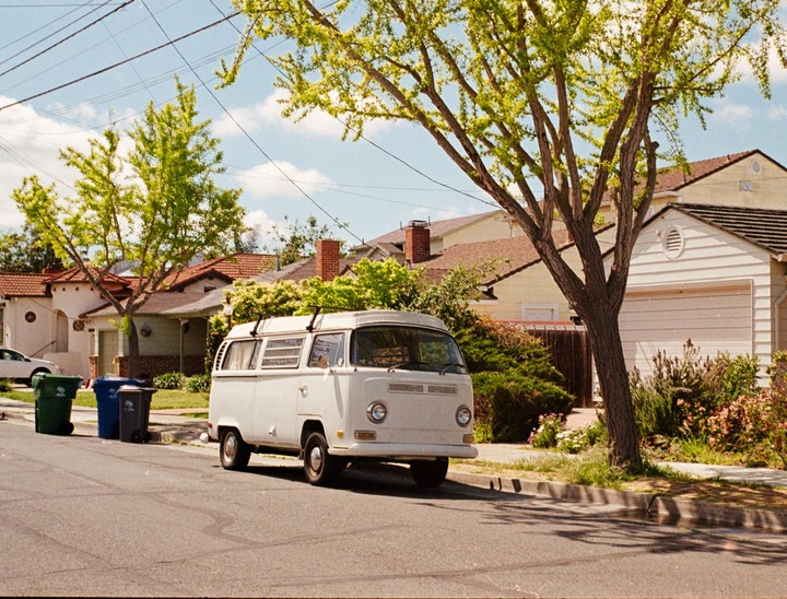A white van is parked on a residential street lined with houses and trees.
