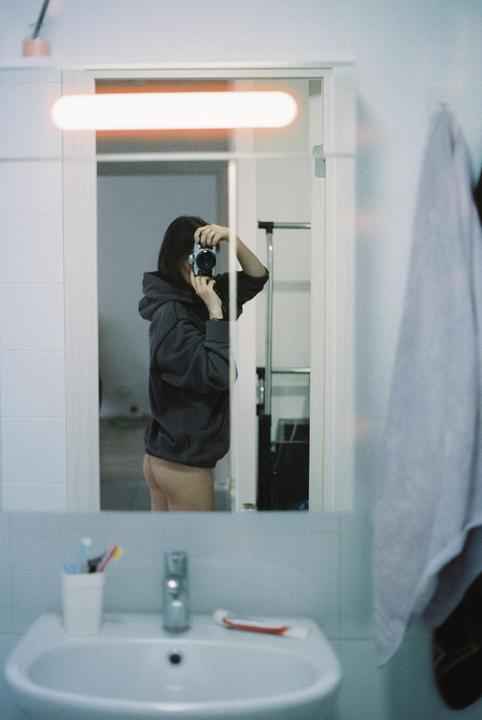 A woman wearing a hoodie takes a mirror self-portrait in a bathroom.