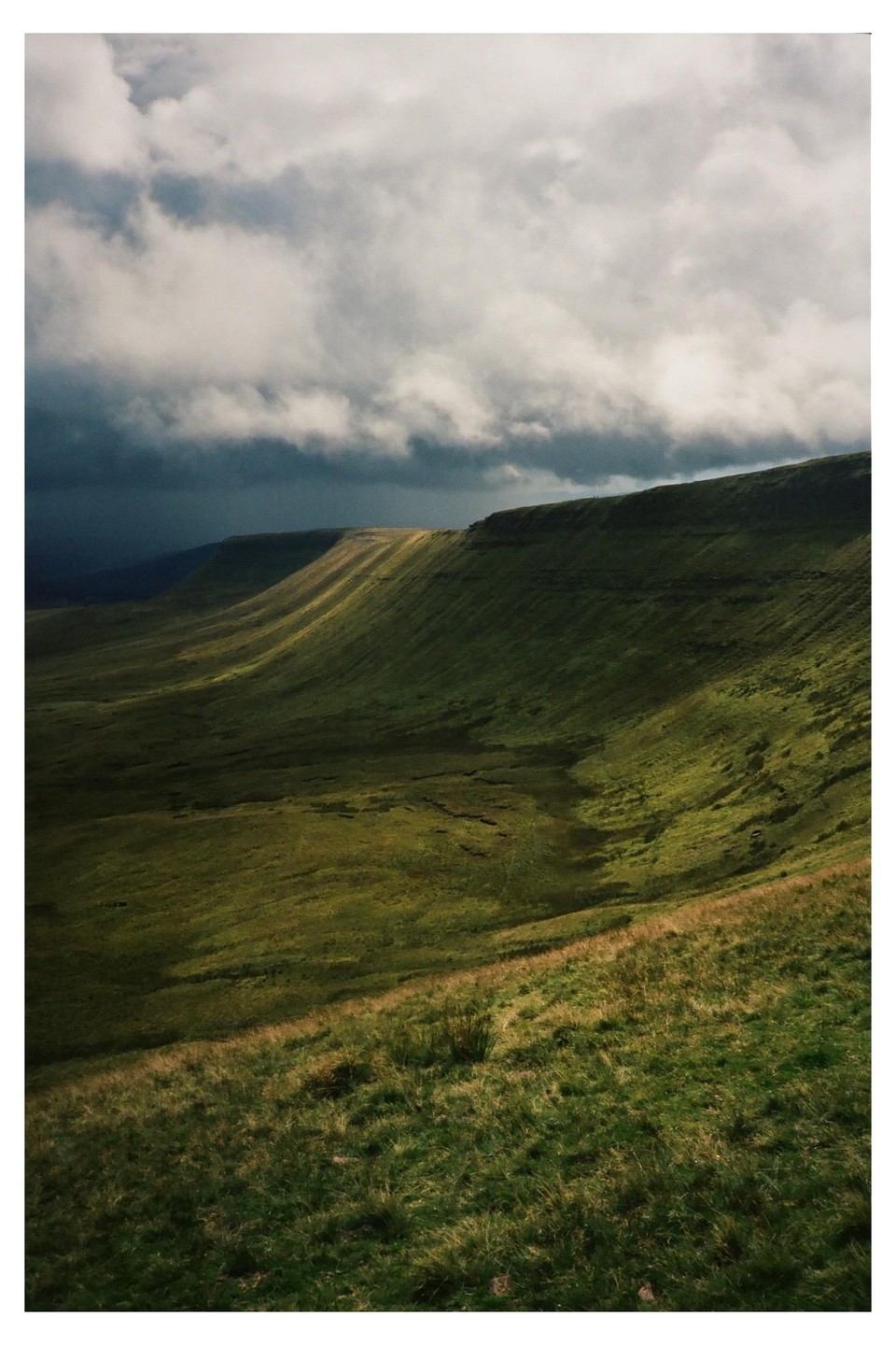 Sunlight illuminates a green mountain range under a cloudy sky.