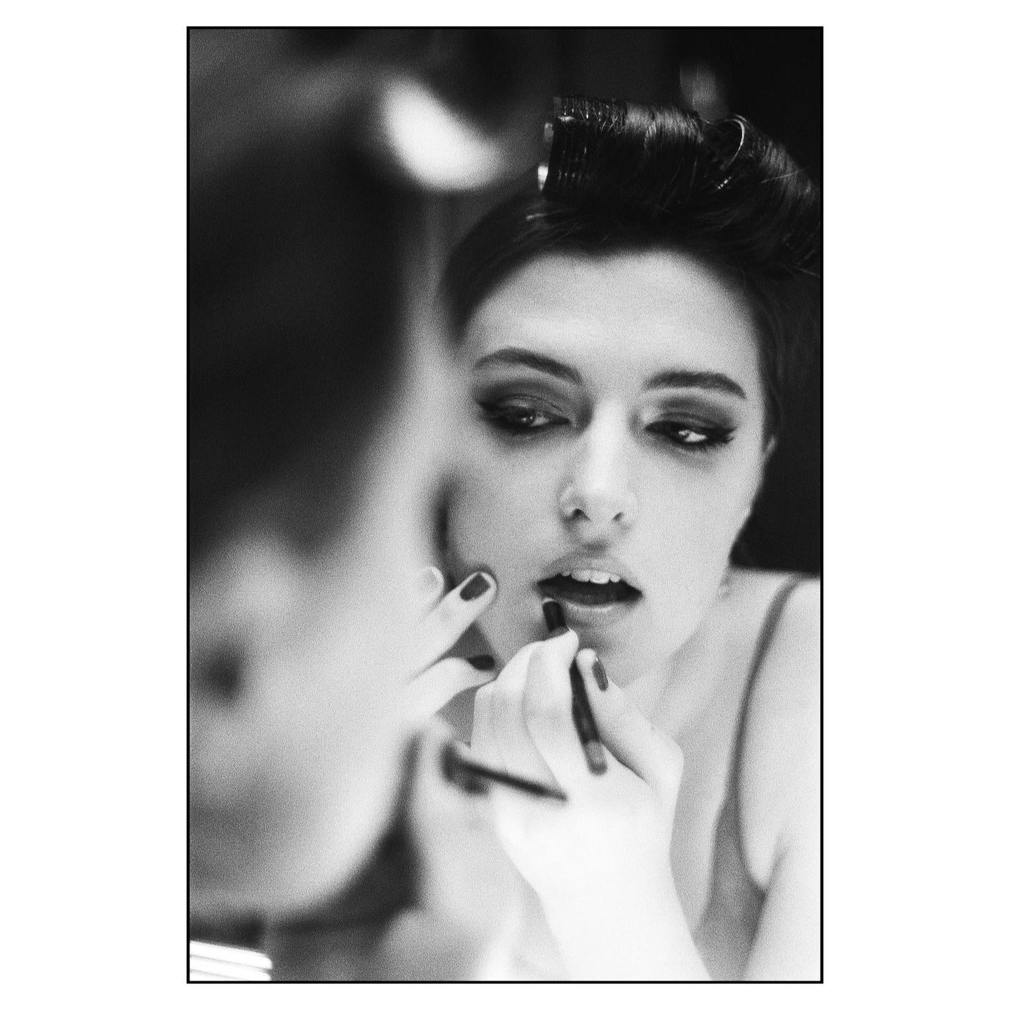 A woman applies makeup to her lips while looking into a mirror.