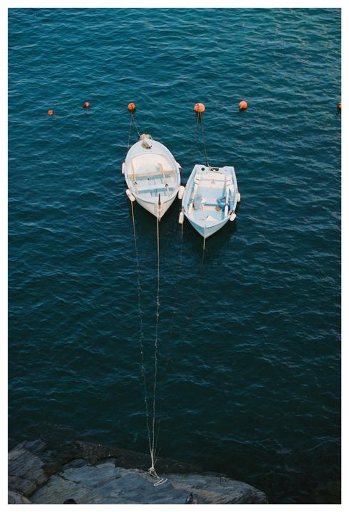 Two small boats are moored in dark blue water next to a rocky shore.