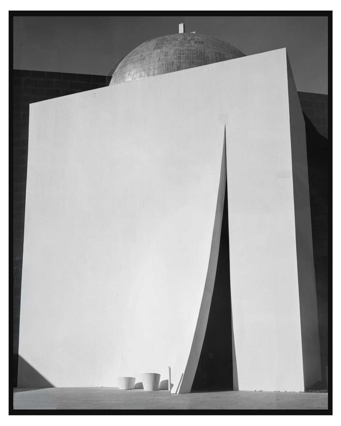 A large white building with a narrow, dark entrance is topped by a domed roof.