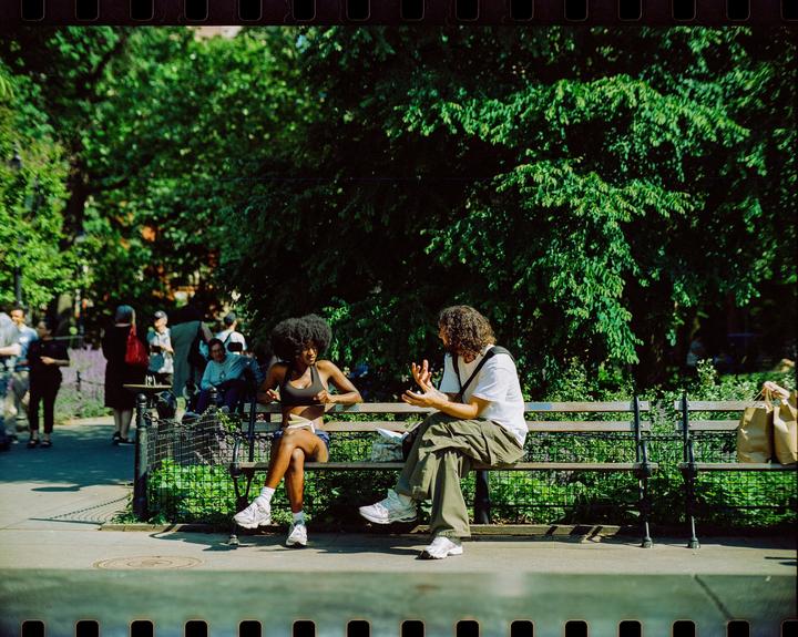 A woman and a man are sitting on a park bench, talking to each other.