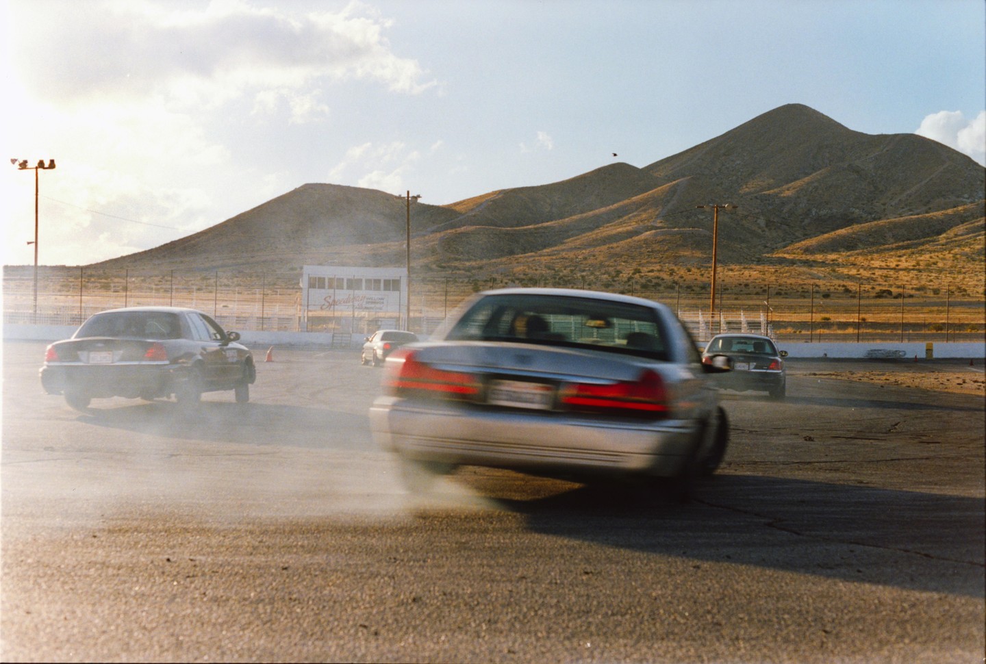 Three cars drift on a track with mountains in the background.