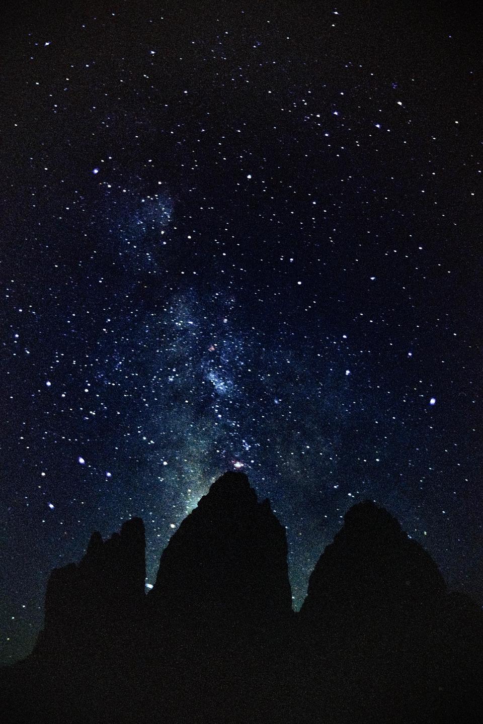 The Milky Way is visible above the dark silhouettes of mountain peaks.