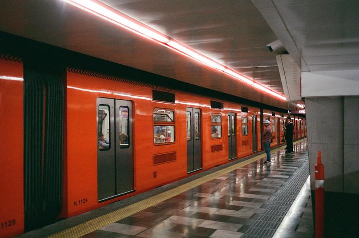 An orange subway train is stopped at a station platform with people waiting and sitting inside.