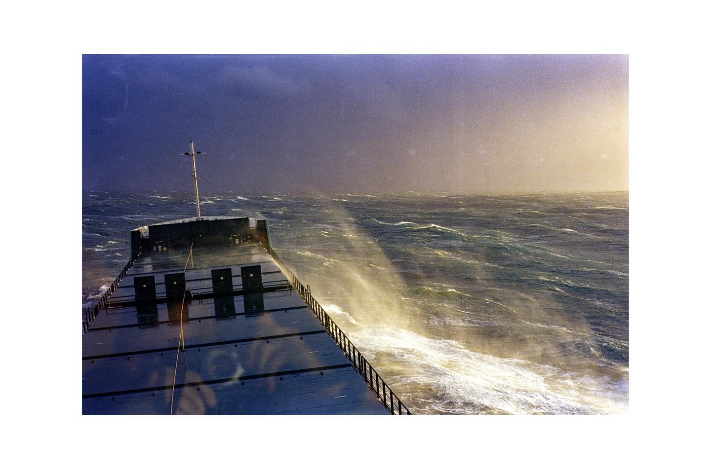 A ship sails through rough seas with spray rising from the waves.