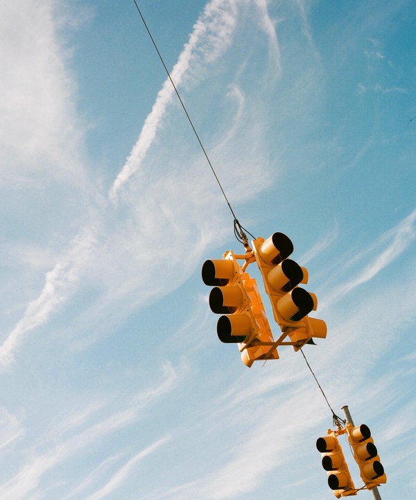 Two yellow traffic lights hang from wires against a blue sky with wispy clouds.