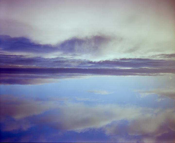Clouds are reflected in a body of water, creating a symmetrical composition.