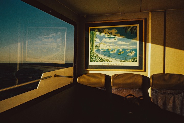 A framed poster of Catalina Island hangs on a wall inside a boat, with the ocean visible through a window.
