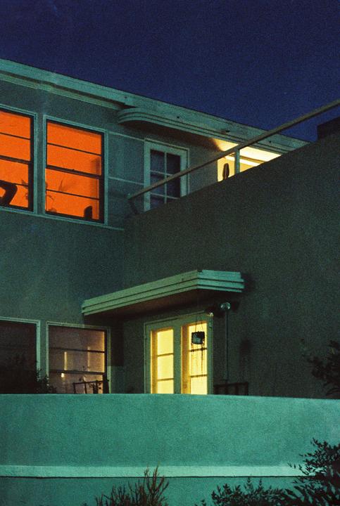 A building with orange and yellow lit windows is seen at night under a dark blue sky.