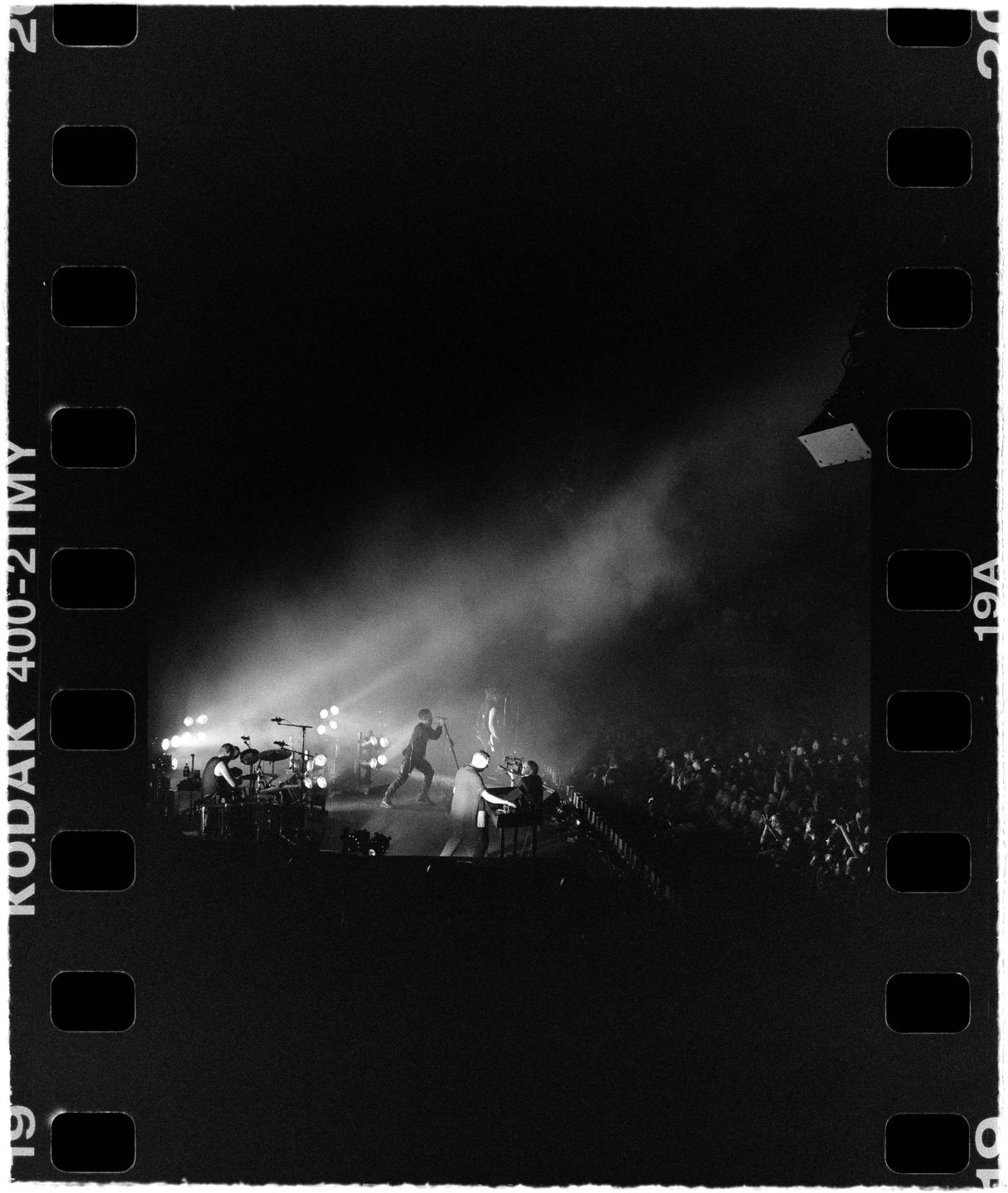 A band performs on a stage illuminated by spotlights in front of a large crowd.