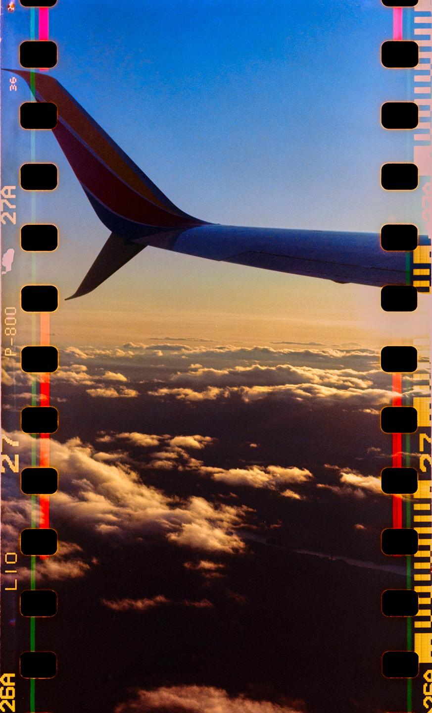 An airplane wing is visible above clouds during sunset.