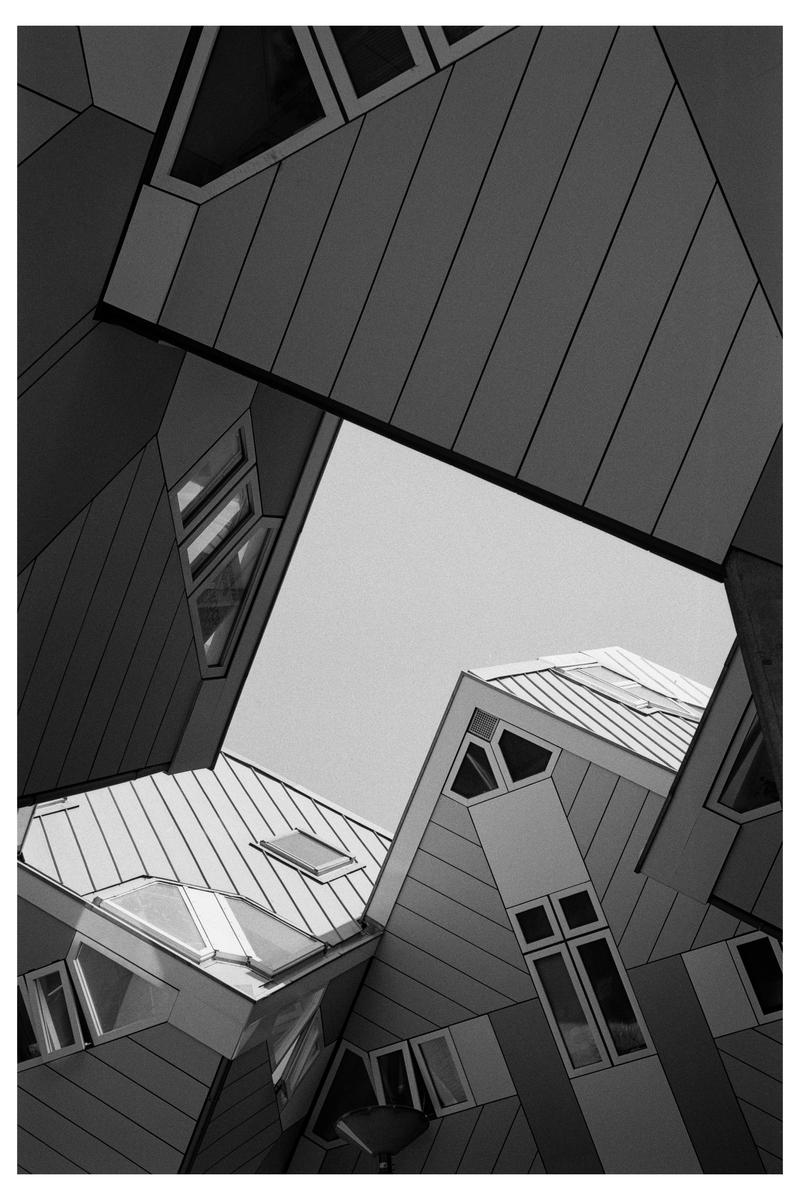 A low-angle black and white shot captures the geometric architecture of the cube houses in Rotterdam.