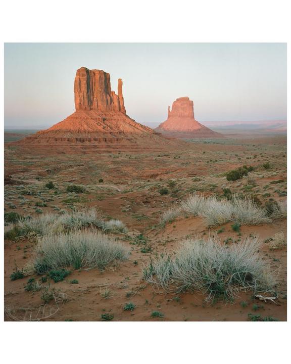 Two large rock formations rise from a desert landscape with sparse vegetation.