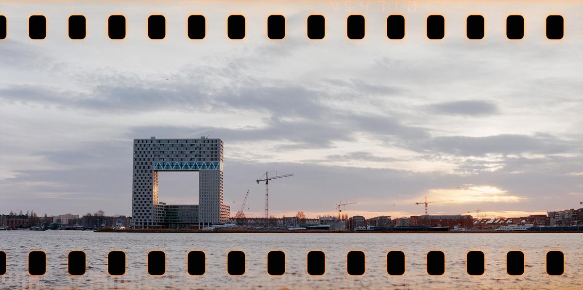 A modern building with a large square opening stands by a body of water under a cloudy sky at dusk.