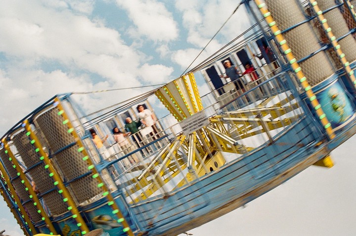 People are riding a spinning carnival ride against a cloudy sky.