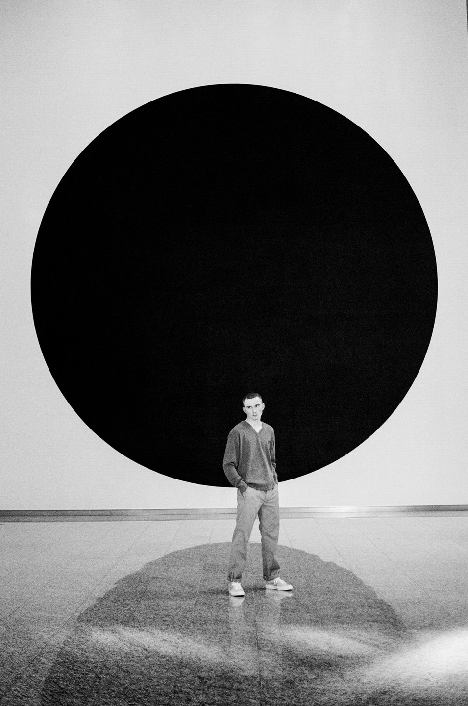 A man stands in front of a large black circle painted on a white wall.