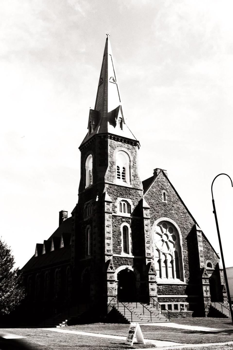 A tall stone church with a prominent steeple stands under a bright sky.