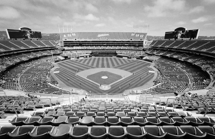 A wide view of a baseball stadium shows the field, stands, and scoreboards under a cloudy sky.