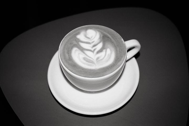 A cup of coffee with latte art sits on a saucer on a dark surface.