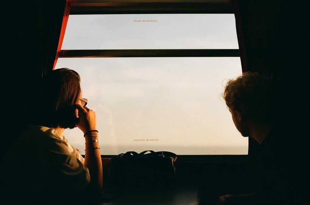 A woman and a man look out a train window at sunset.