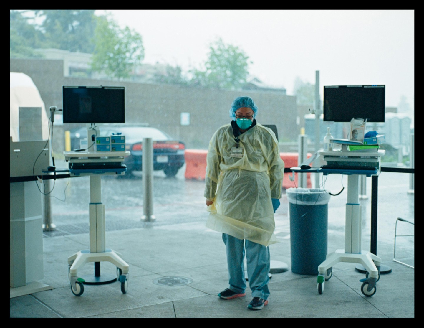 A woman in personal protective equipment stands between two medical carts with monitors.