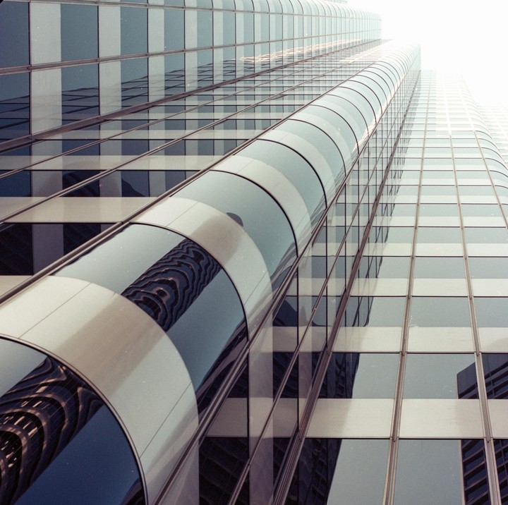 A tall building with a curved glass facade reflects another building.