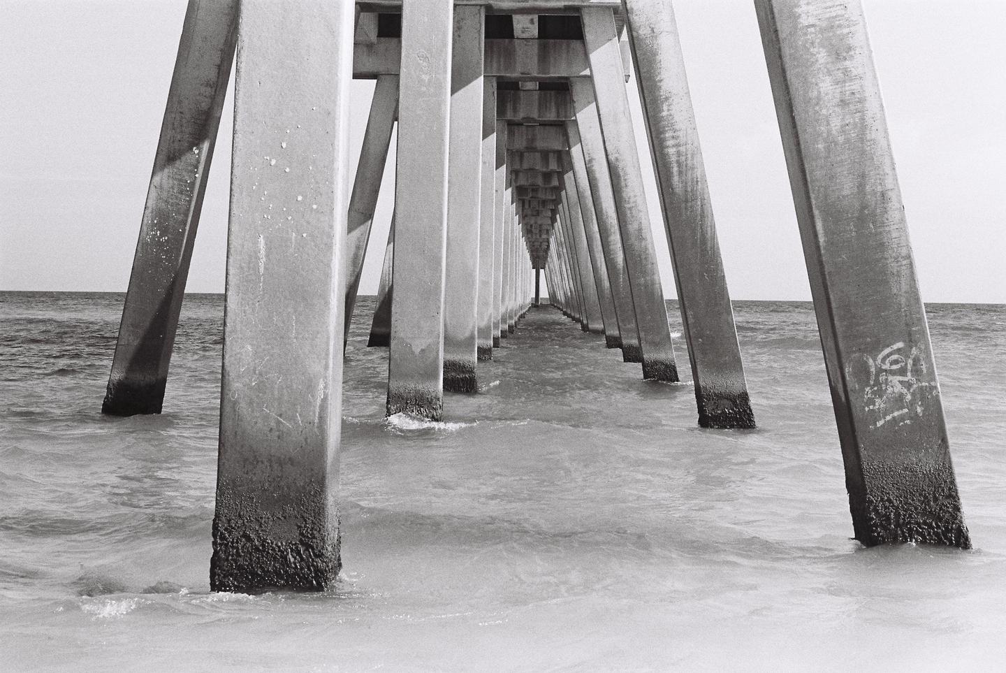The concrete pillars of a pier extend into the distance over the ocean.