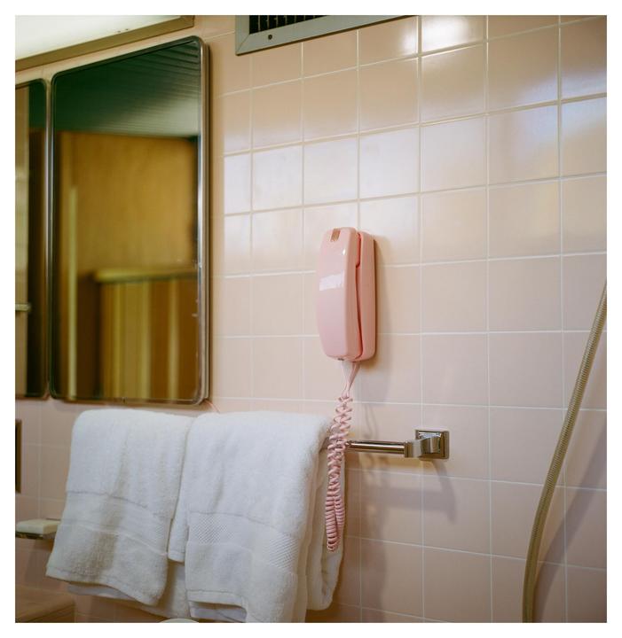 A pink wall-mounted telephone hangs above a towel rack with two white towels in a bathroom with pink tiled walls.