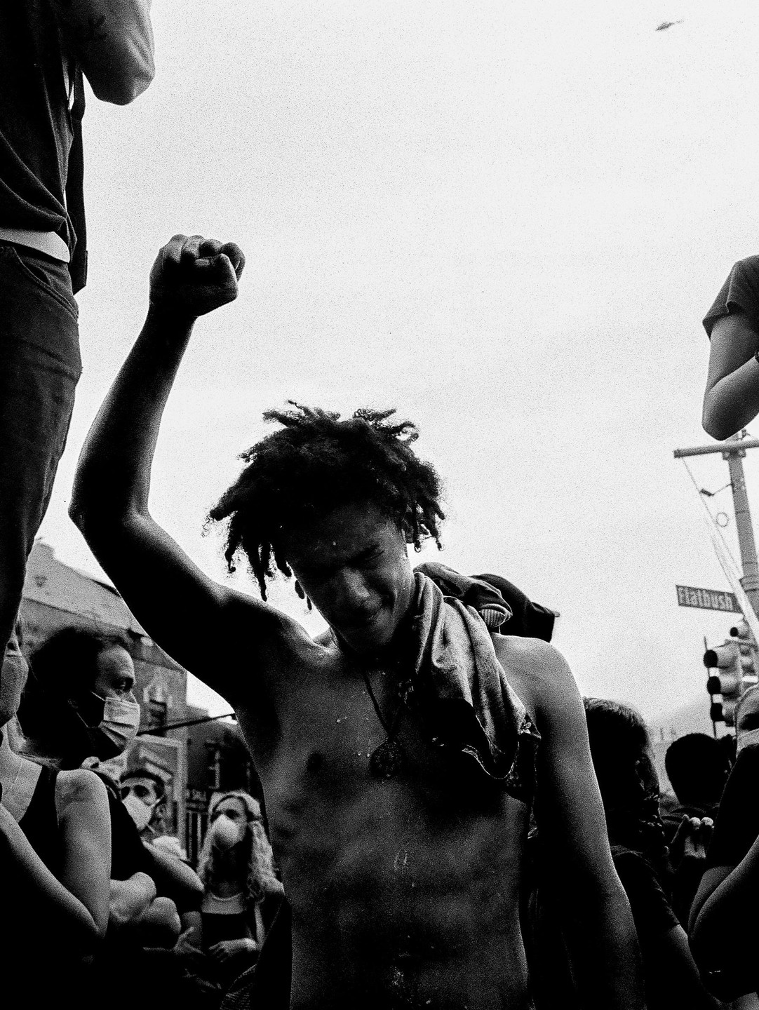 A shirtless man with dreadlocks raises his fist in the air during a protest on Flatbush Avenue.