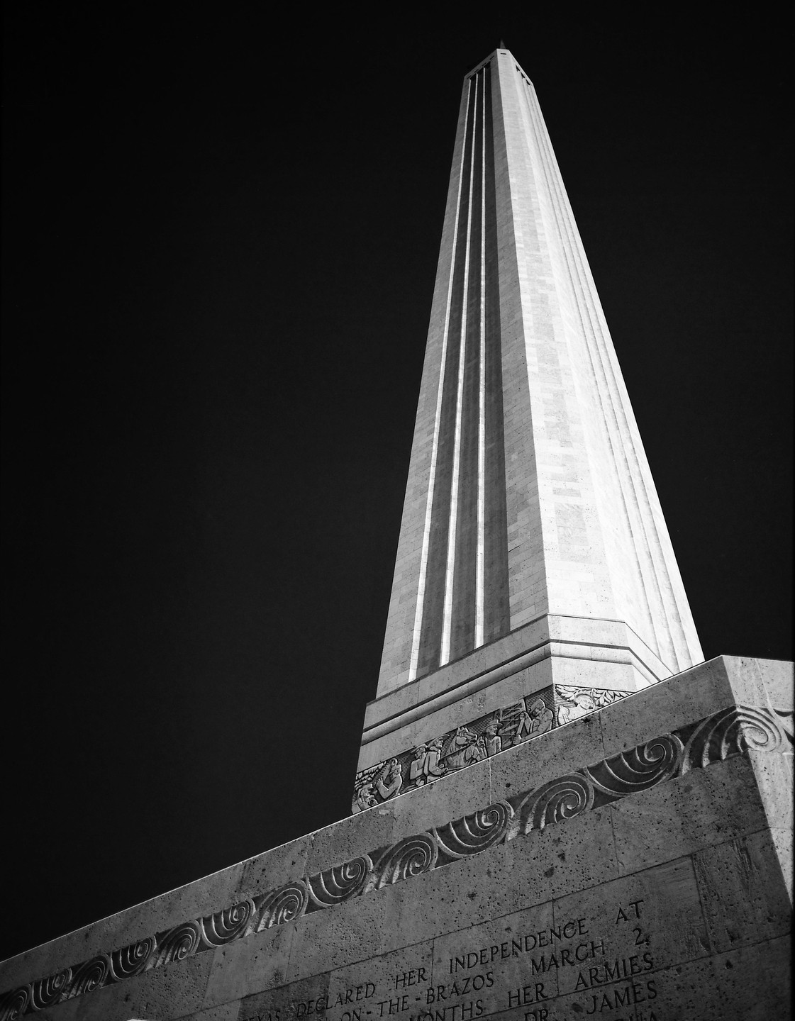 A tall, narrow monument with a decorative base stands against a dark sky.