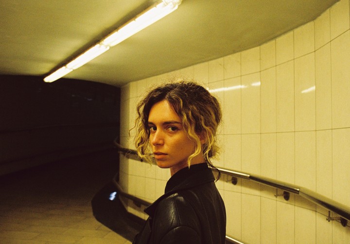 A woman with curly hair looks over her shoulder in a subway tunnel with fluorescent lighting.