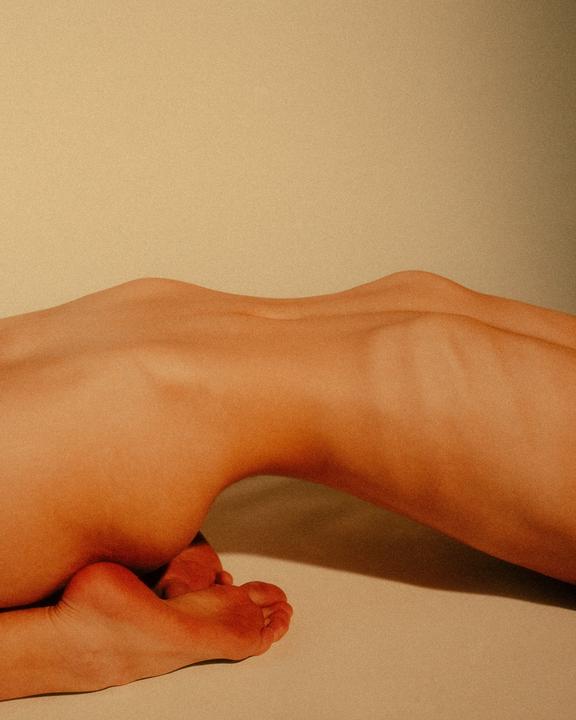 A person is lying on their stomach with their feet tucked under them, creating a silhouette against a light background.