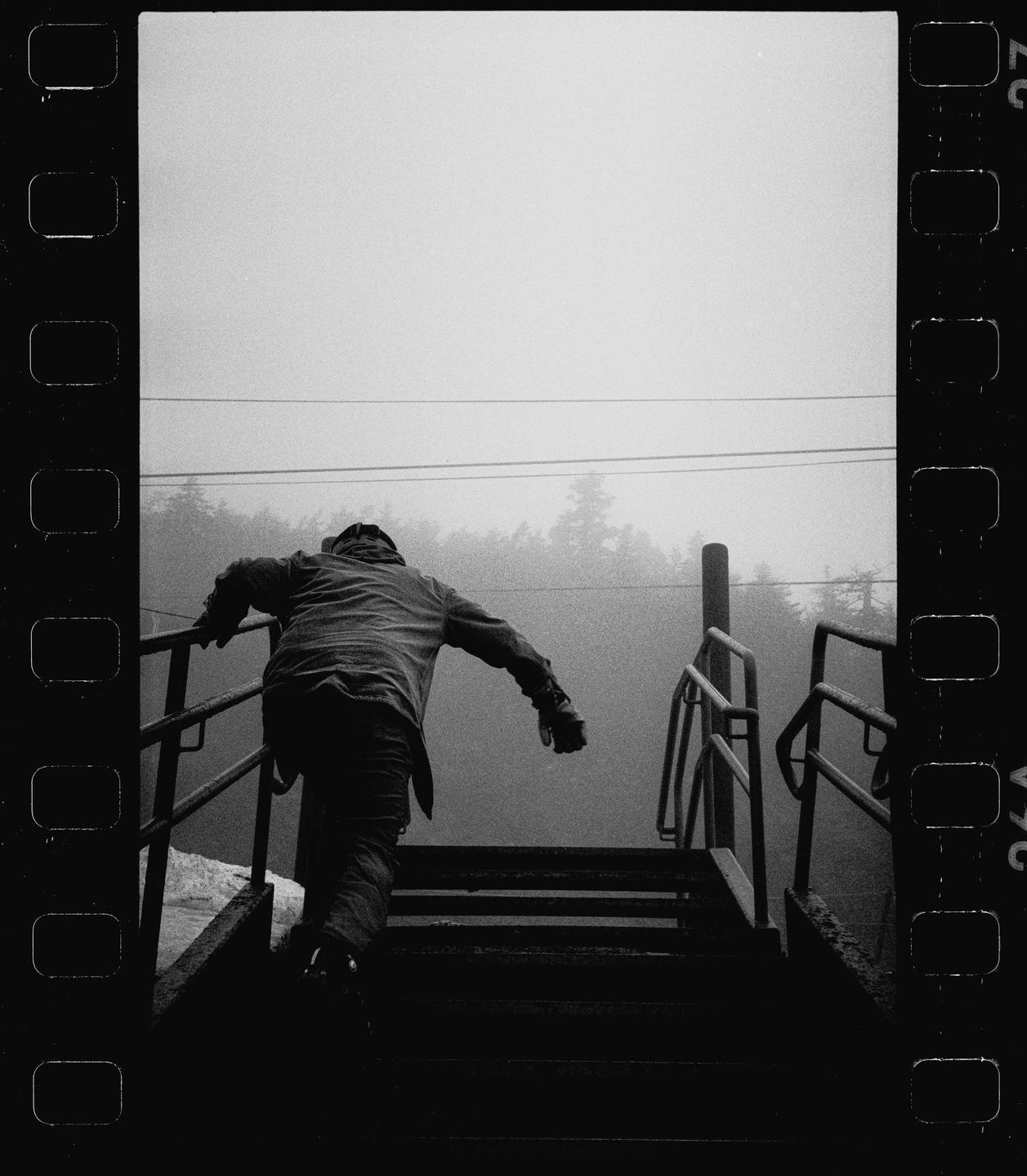A person climbs a set of outdoor stairs with railings into a hazy, tree-lined background.