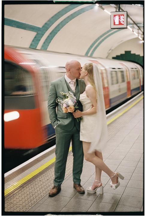 A couple kisses on a subway platform as a train passes by.