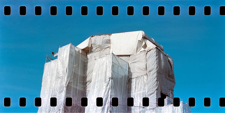 A building under construction is covered in white tarps against a clear blue sky.