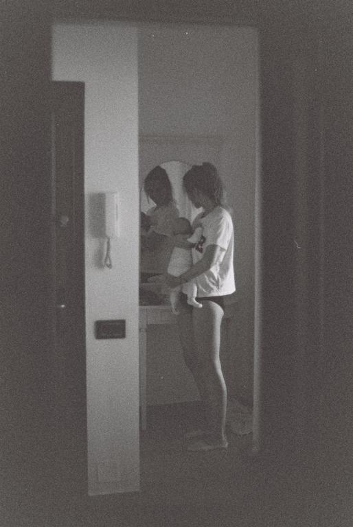 A woman holds a baby in a room with a mirror reflecting their figures.