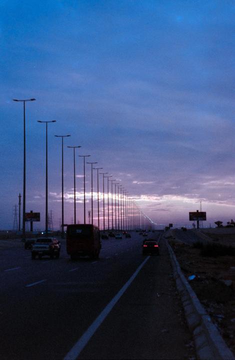 A long road with many streetlights and cars is visible under a dramatic purple and blue sky at dusk.