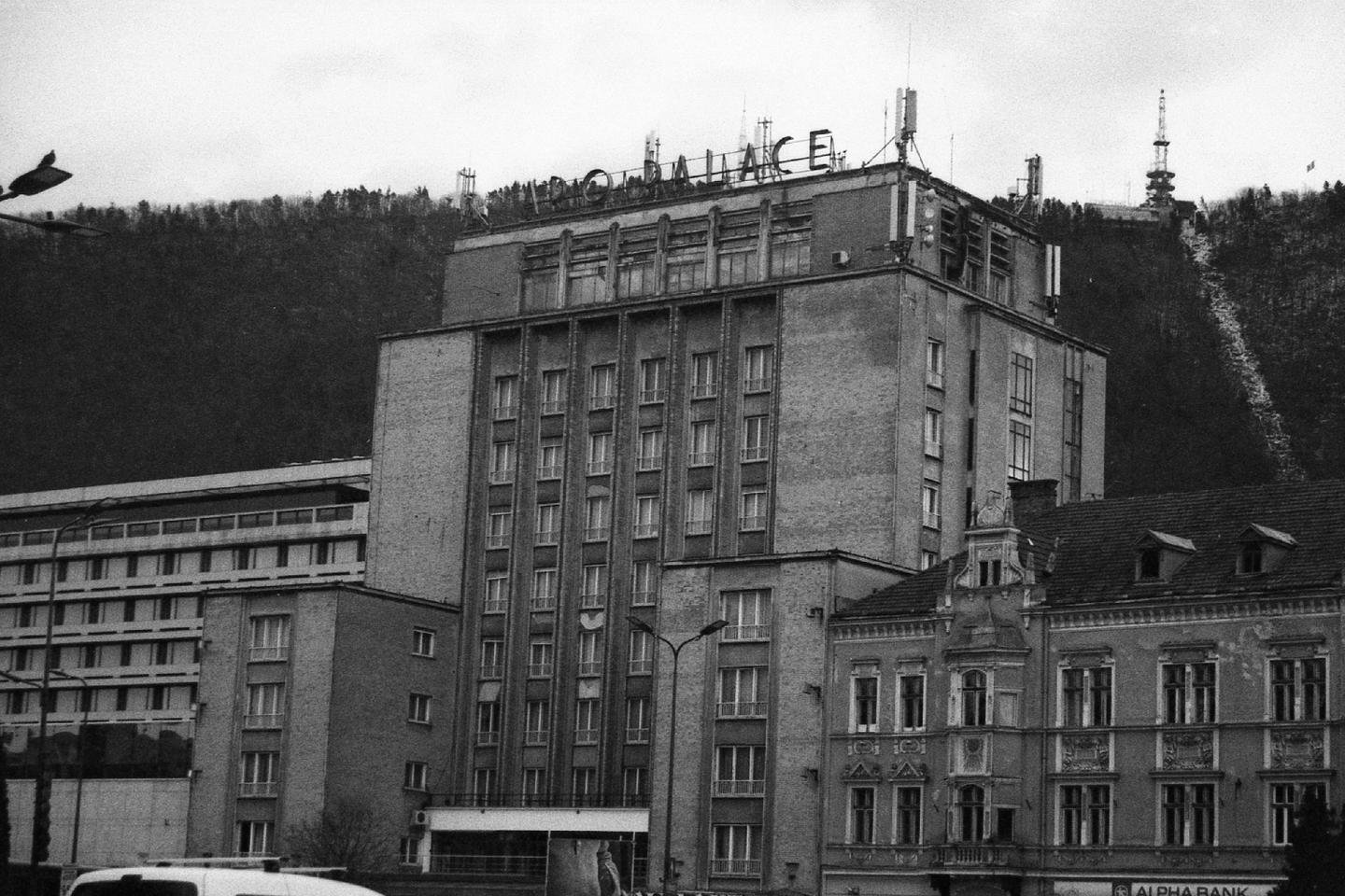 A large building with "PALACE" written on its roof stands in front of a forested hill with a transmission tower.