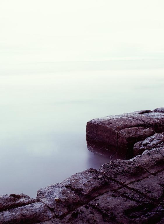 A long exposure captures the smooth surface of the ocean next to dark, textured rocks.
