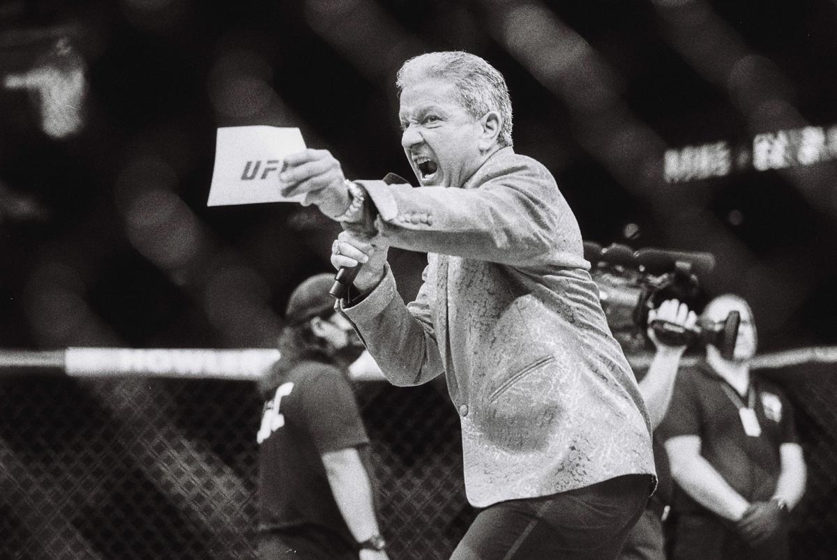 A man in a patterned jacket shouts into a microphone while holding a piece of paper with "UF" written on it.