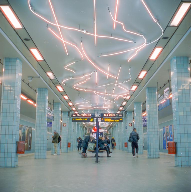 People wait for a train in the brightly lit underground station with blue tiled walls.