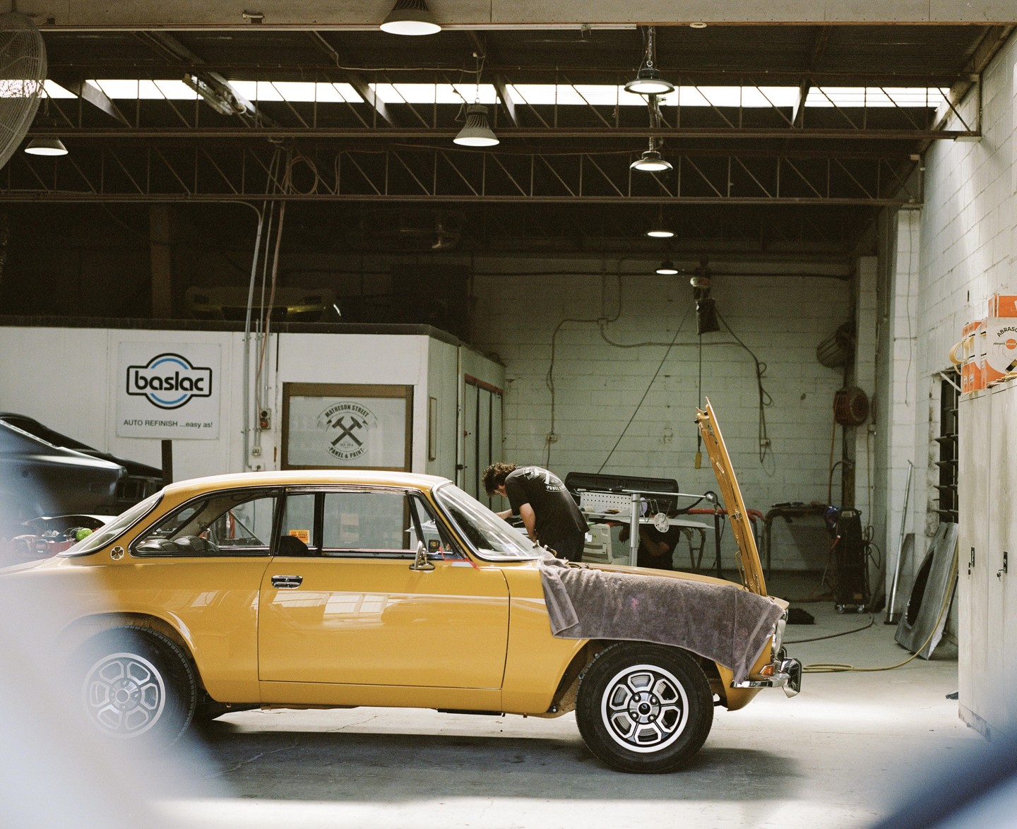 A man works on a yellow car with its hood open in a garage.