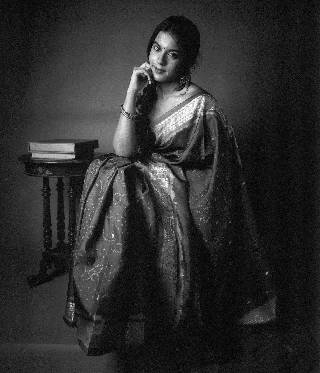 A woman in a sari sits next to a small table with books.