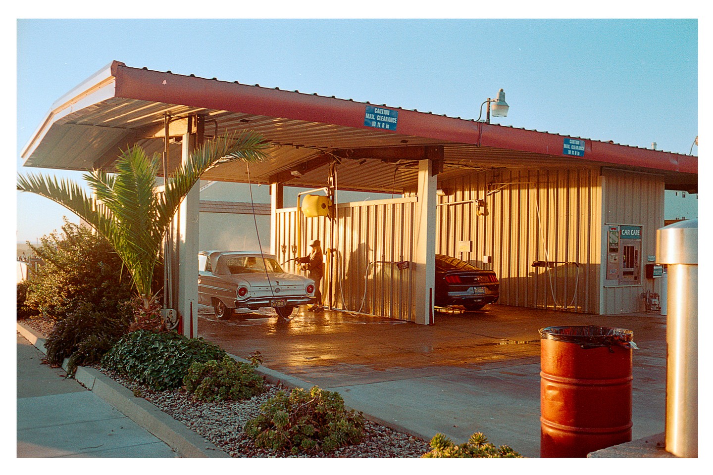 A man washes a silver car at a car wash during golden hour.