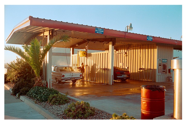 A man washes a silver car at a car wash during golden hour.